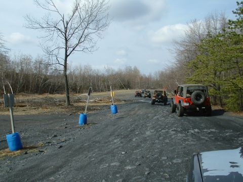 1991 Ford Bronco - A convoy of Jeeps travels down a dirt road through a wooded area on an overcast day.
