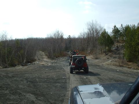 1991 Ford Bronco - A line of Jeeps navigates a rough dirt path through a wooded area on a cloudy day.