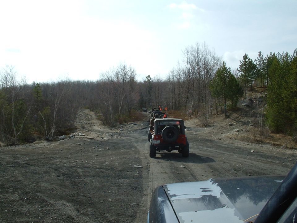 Red Jeep Wrangler with spare tire on rear door, driving on a dirt road with trees