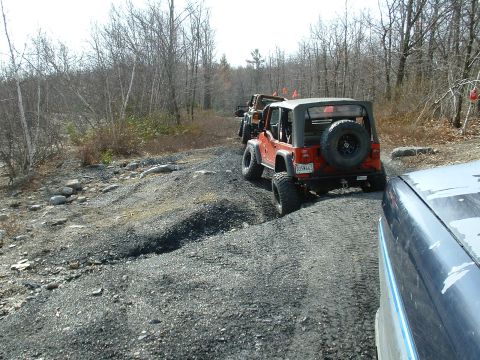 1991 Ford Bronco - A line of Jeeps navigates a rough, gravelly trail through a wooded area.