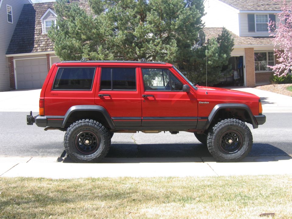 Red Jeep Cherokee XJ four-door lifted on black wheels parked in a residential driveway