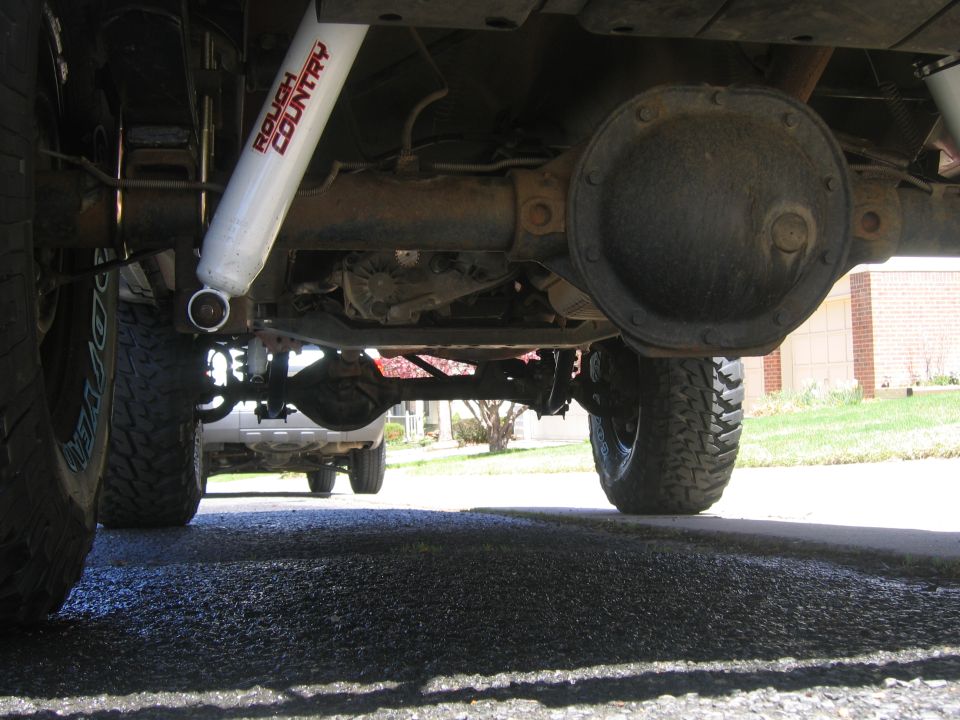 Underbody view of a lifted truck showing rear axle and white Rough Country shock absorber