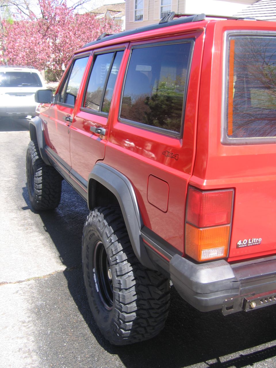 Rear quarter of lifted red Jeep Cherokee XJ on black steel wheels and mud tires