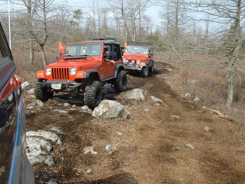 1991 Ford Bronco - Two Jeep Wranglers navigate a challenging rocky off-road trail through a wooded area.