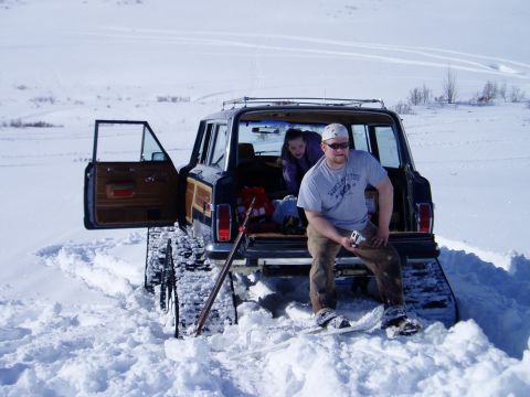2000 Ford E350 - A Jeep Grand Wagoneer equipped with snow tracks sits in a snowy landscape with two people.