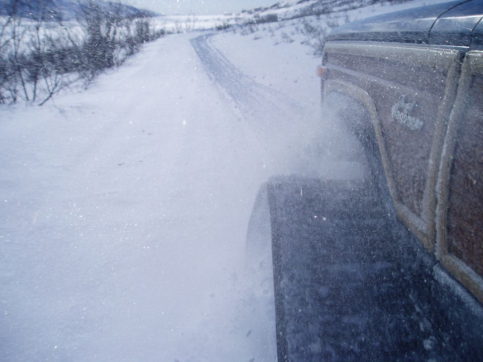 Wood-paneled SUV side view, kicking up snow on a winter road