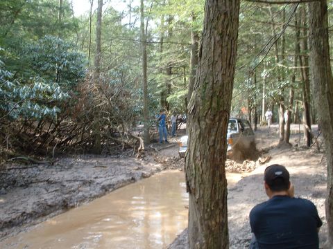 1991 Ford Bronco - Multiple vehicles navigate a muddy trail in a wooded area.