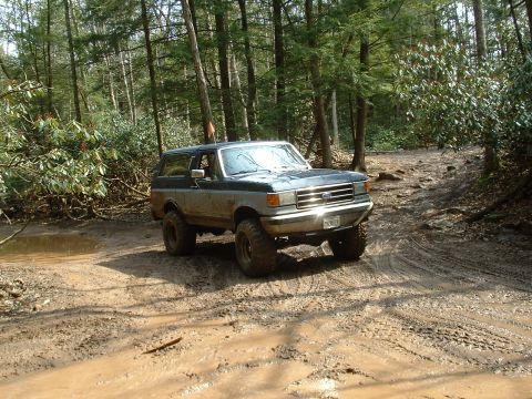 1991 Ford Bronco - This 1991 Ford Bronco navigates a challenging muddy path in a wooded area.