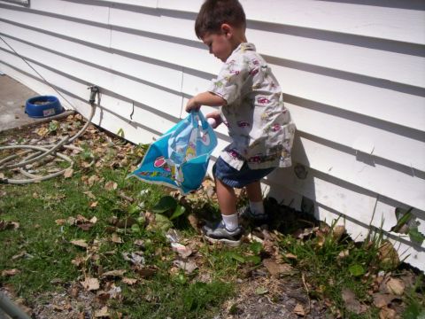 1986 Ford Bronco - A young boy dressed in a patterned shirt and denim shorts collects Easter eggs in a blue bag near a white house.