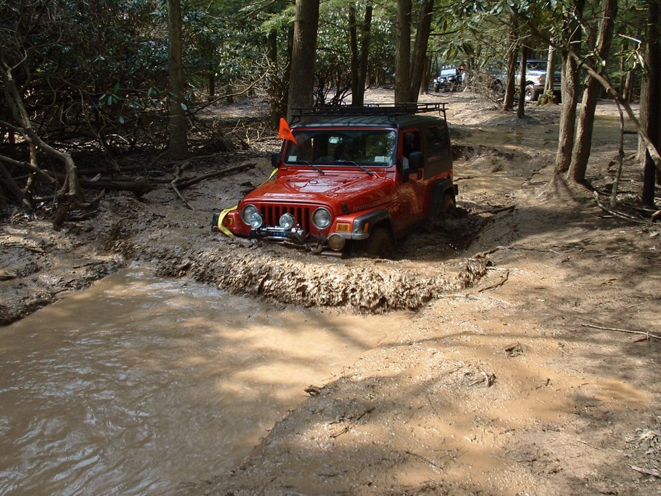 Red Jeep Wrangler stuck in mud, with other vehicles in background