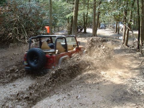 1991 Ford Bronco - Off-roading through a muddy trail in a forest with another vehicle in the distance.