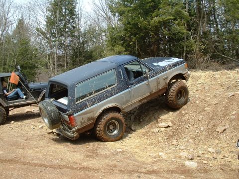 1991 Ford Bronco - A muddy Ford Bronco navigates an off-road trail alongside another vehicle.