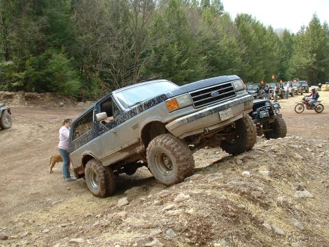 1991 Ford Bronco - A lifted Ford Bronco navigates an off-road trail with other vehicles in the background.