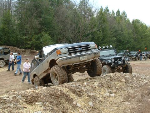 1991 Ford Bronco - A lifted 1991 Ford Bronco navigates an off-road obstacle course with other vehicles in the background.