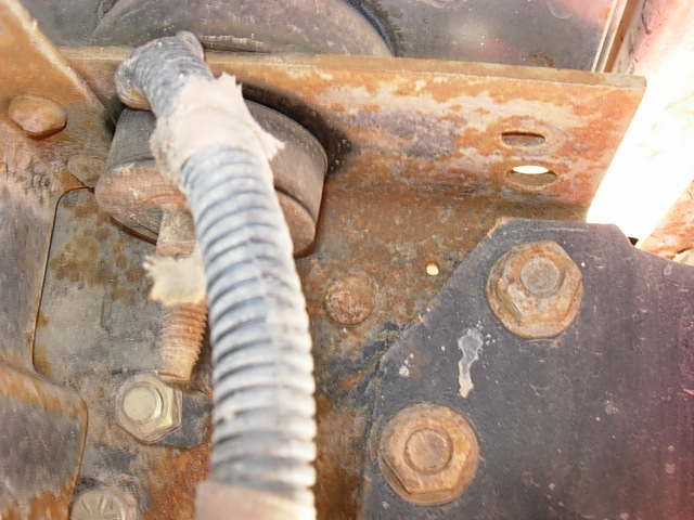 Rusted metal bracket with bolts and a gray wire conduit, showing signs of wear and tear