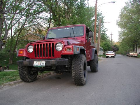 1998 Jeep TJ - A red 1998 Jeep TJ is parked on a residential street, viewed from the front. A sticker on the windshield reads KCJeepClub.org.