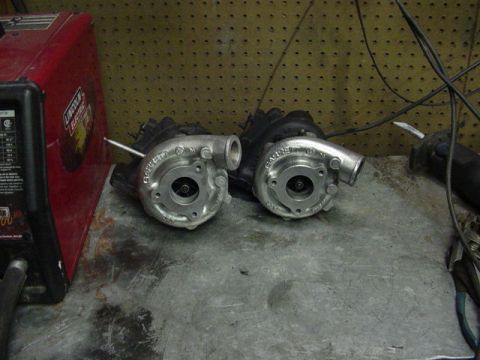 1995 Ford Mustang - Two Garrett turbochargers are displayed on a metal surface, with a red welding machine to the left.