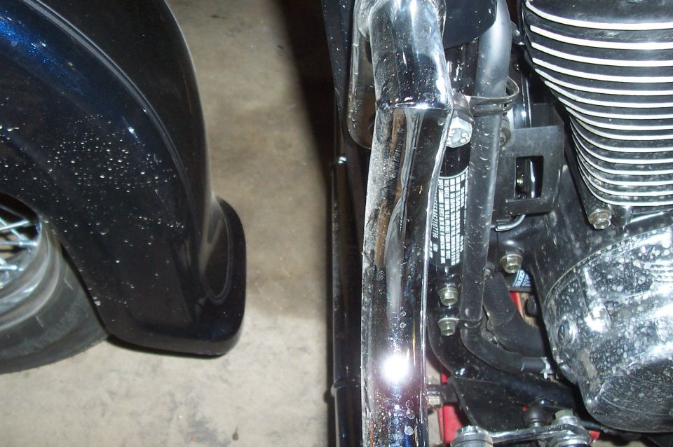 Close-up of motorcycle engine fins, chrome pipes, and part of a black fender