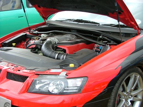 2001 Ford Fiesta - The engine bay of a red and black car, a prominent supercharger. Another vehicle is partially visible on the left.