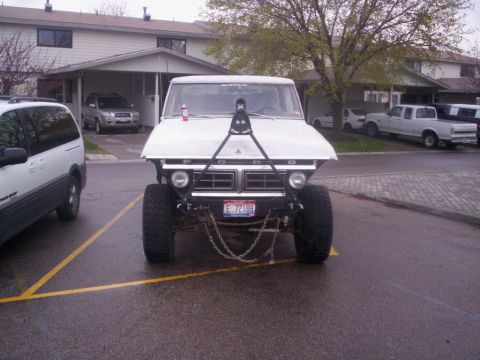 1978 Ford Bronco - A lifted 1978 Ford Bronco is parked in front of a residential building, its front end dominated by large tires and decorative chains.