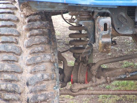 1989 Ford Bronco - Muddy suspension and tire of an off-road vehicle, likely modified for off-roading.