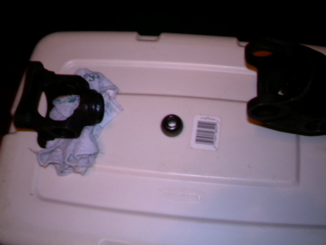 Driveshaft part with a rag, a small black ring, and a barcode sticker on a white plastic storage bin