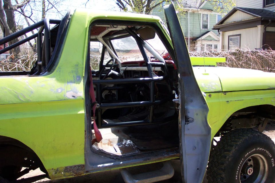 1978 Ford Bronco interior showing extensive rollcage and open driver's door