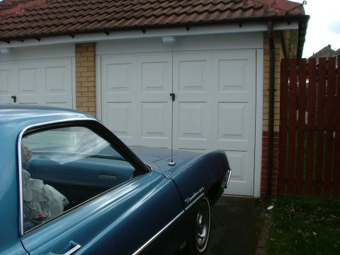 1970 Ford Ranchero - A blue 1970 Ford Ranchero is parked in front of a white garage door with a red wooden fence to the right.