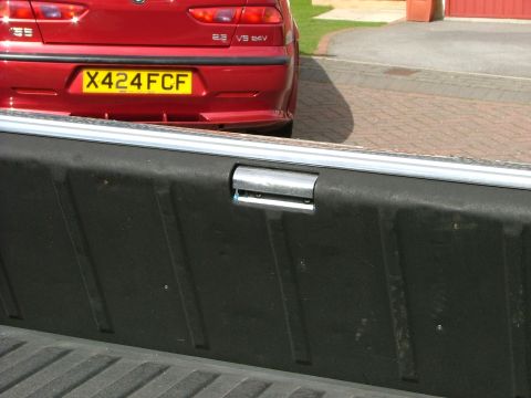 1970 Ford Ranchero - A red sedan is visible behind the bed of a pickup truck, showing its rear bumper and license plate.
