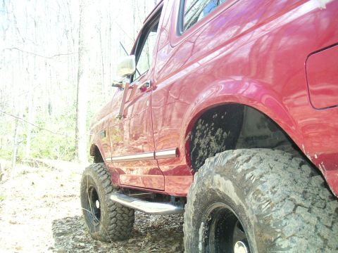 1994 Ford Bronco - This red SUV, likely from the early to mid-1990s, is equipped for off-road use with large tires.