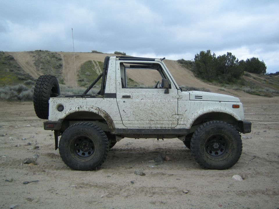 1987 Suzuki Samurai side view, covered in mud, parked on dirt with hills in background