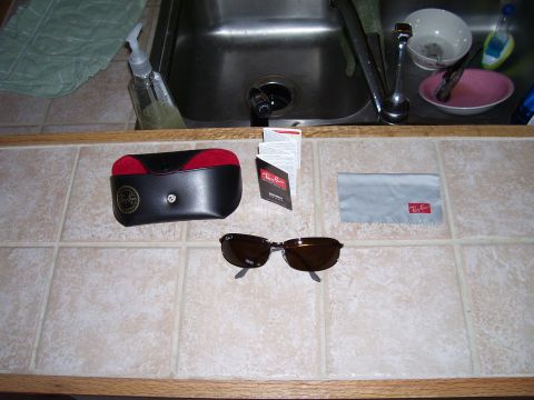 1992 Ford Bronco - Ray-Ban sunglasses, case, and cleaning cloth are laid out on a tiled surface next to a kitchen sink.