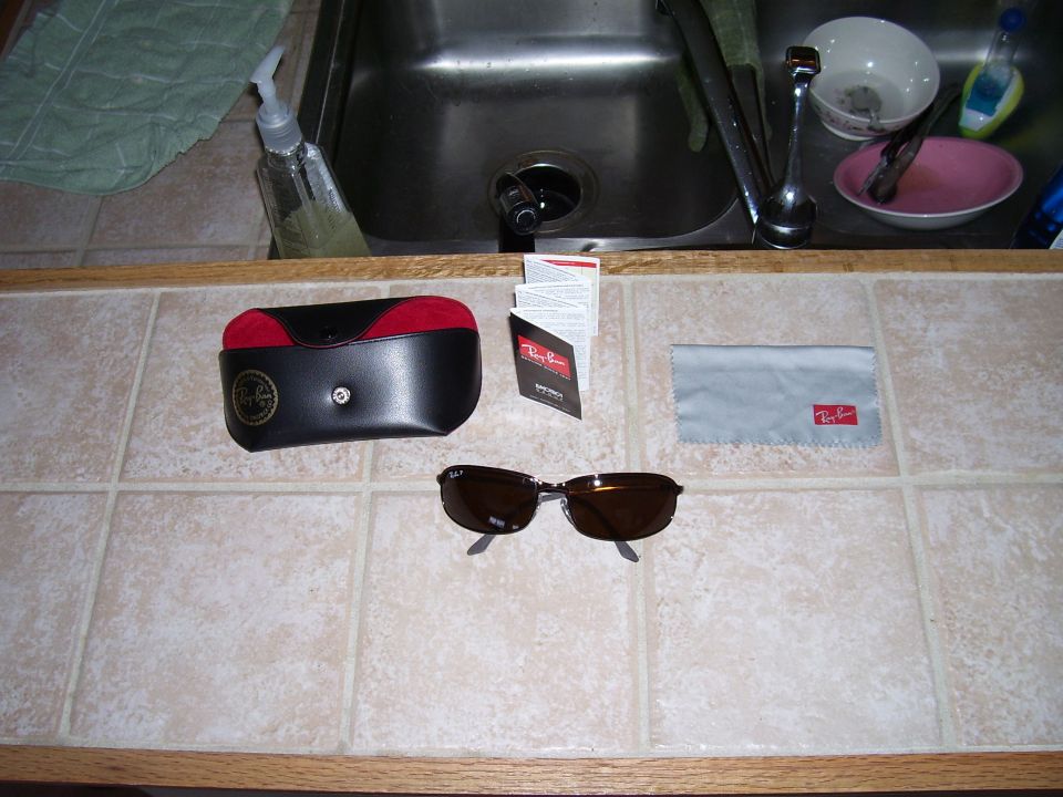 Brown Ray-Ban sunglasses with case and cleaning cloth on a tiled countertop