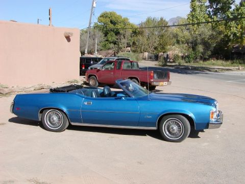1973 Mercury Cougar - A blue 1973 Mercury Cougar convertible is parked next to a red pickup truck.