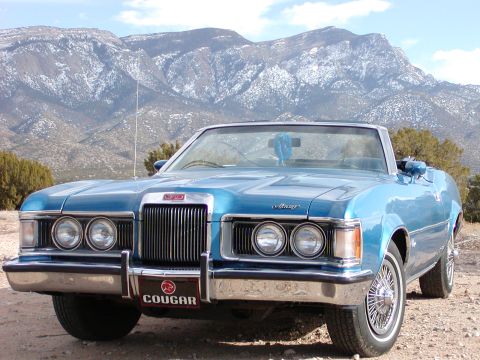 1973 Mercury Cougar - A blue 1973 Mercury Cougar convertible is parked in front of a snow-capped mountain range.