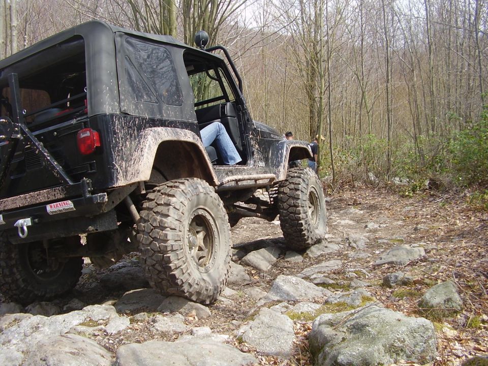 Black Jeep Wrangler on a rocky trail, going over large stones. Person inside wearing blue jeans
