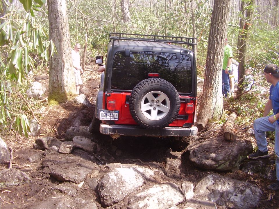 Red Jeep Wrangler navigating a rocky trail with people watching