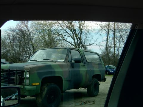 2001 Ford Crown Victoria - A camouflage SUV is parked outside with trees and another vehicle visible in the distance.