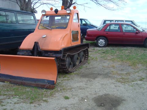 2001 Ford Crown Victoria - An orange tracked vehicle with a front plow is parked outdoors next to several cars.