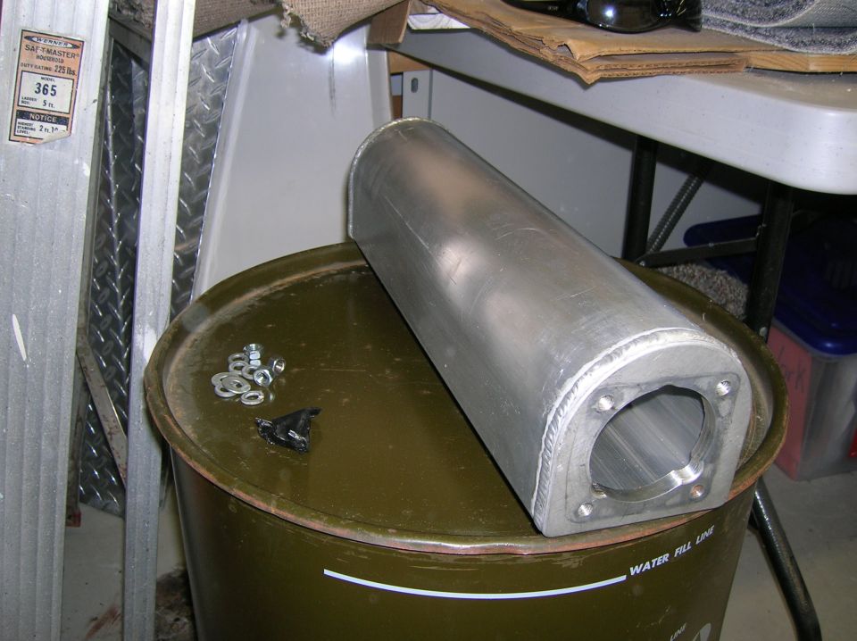 Aluminum exhaust tip with mounting holes sits on a green barrel next to nuts and washers