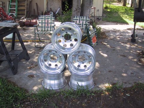 1990 Ford Bronco - A collection of aluminum wheels is displayed outdoors, with various items in the background.