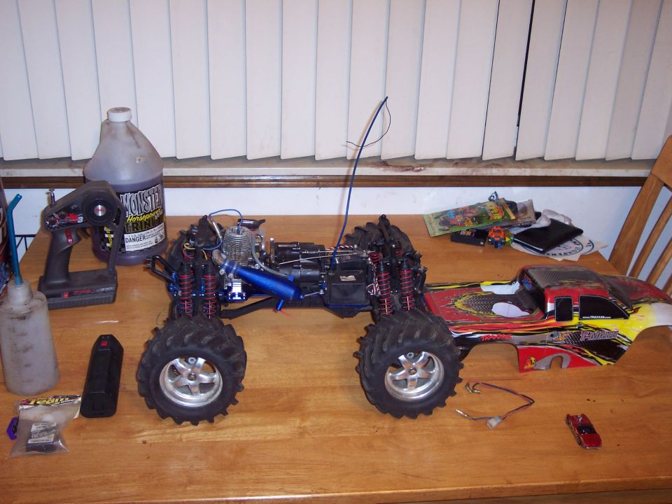 Remote-controlled monster truck with a detached body, on a wooden table with a controller and fuel bottle