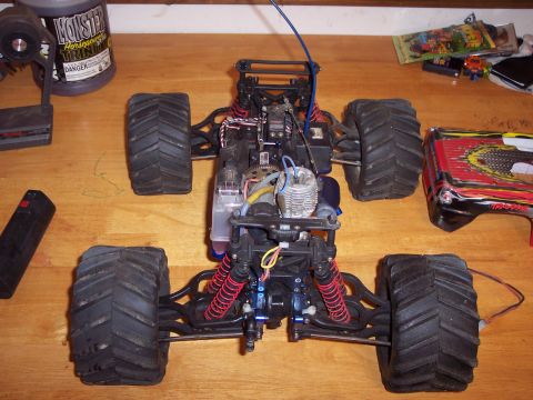 1974 Ford Bronco - The chassis of a remote control monster truck, a nitro engine, suspension, and oversized tires, is displayed on a wooden surface.