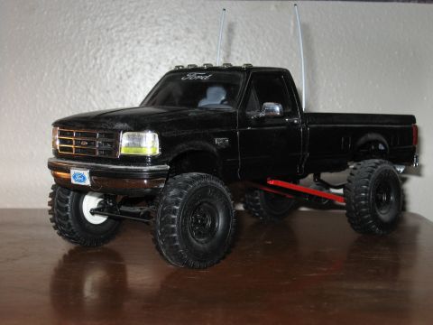 1977 Ford F-150 - detailed black Ford F-series die-cast model pickup with a suspension lift, roll bar lights and chrome grille on a wood surface.