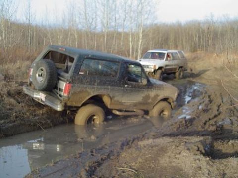 1995 Ford Bronco - Two off-road vehicles navigate a challenging muddy terrain, with one vehicle deeply mired.