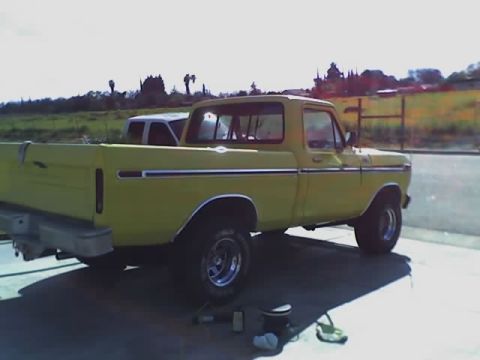 1996 Ford Bronco - A yellow pickup truck is parked on a driveway with a grassy field and trees in the background.