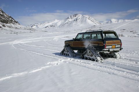 2003 Jeep TJ - A Jeep Grand Wagoneer equipped with tracks drives through a snowy landscape with mountains in the background.