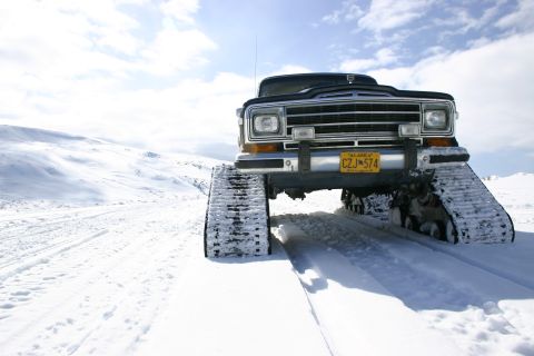 2003 Jeep TJ - A Jeep Cherokee equipped with snow tracks navigates a snowy landscape under a bright sky.