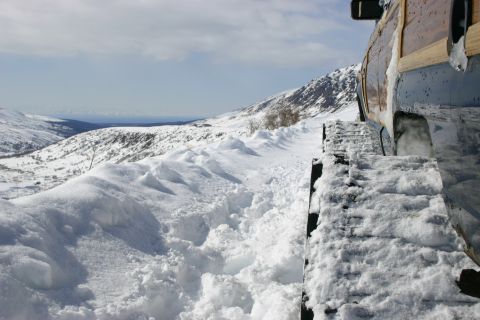 2003 Jeep TJ - A vehicle equipped with tracks navigates a snow-covered mountain path under a cloudy sky.