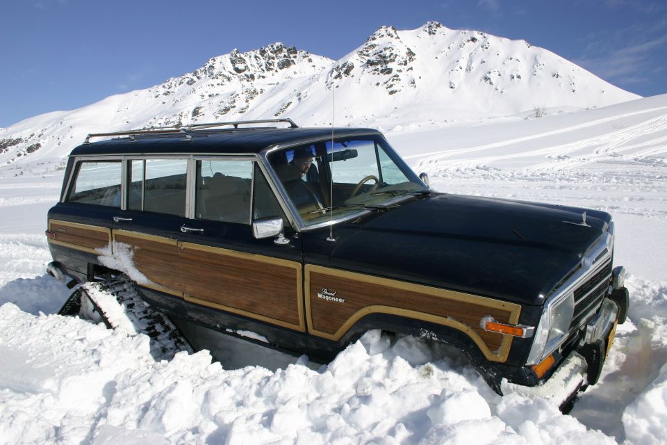 Black woodgrain Jeep Grand Wagoneer stuck in deep snow with mountains behind
